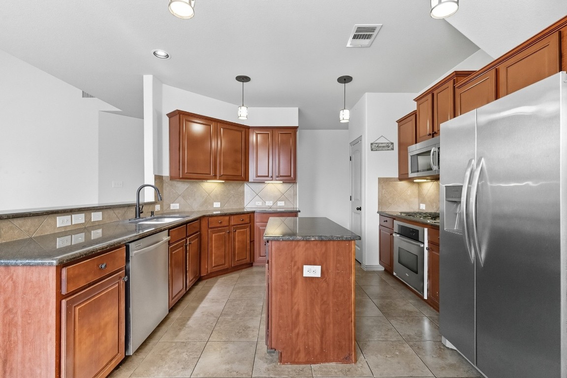 2409 Pauma Valley Way Pflugerville, TX 78660 - Photo 12 of 37 Kitchen with stainless steel appliances, decorative backsplash, hanging light fixtures, light tile patterned floors, and a kitchen island