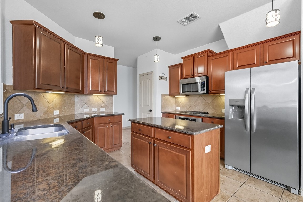 2409 Pauma Valley Way Pflugerville, TX 78660 - Photo 13 of 37 Kitchen featuring stainless steel appliances, hanging light fixtures, light tile patterned flooring, and dark stone countertops
