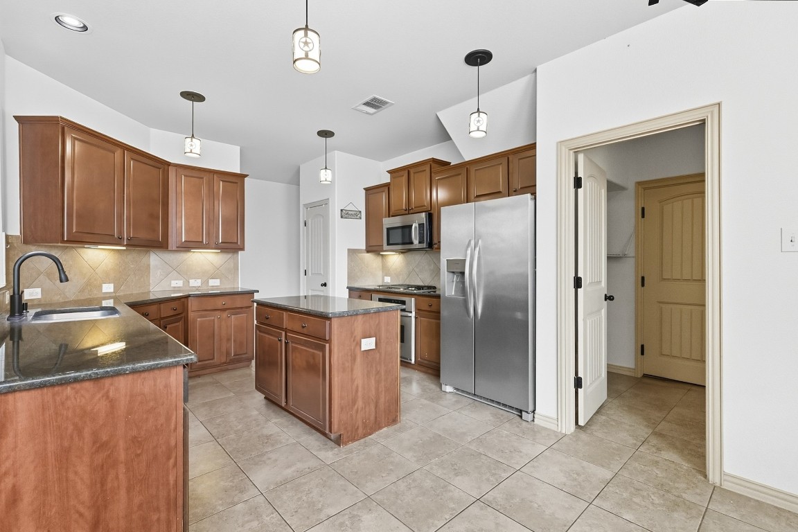 2409 Pauma Valley Way Pflugerville, TX 78660 - Photo 10 of 37 Kitchen featuring appliances with stainless steel finishes, hanging light fixtures, decorative backsplash, and brown cabinets