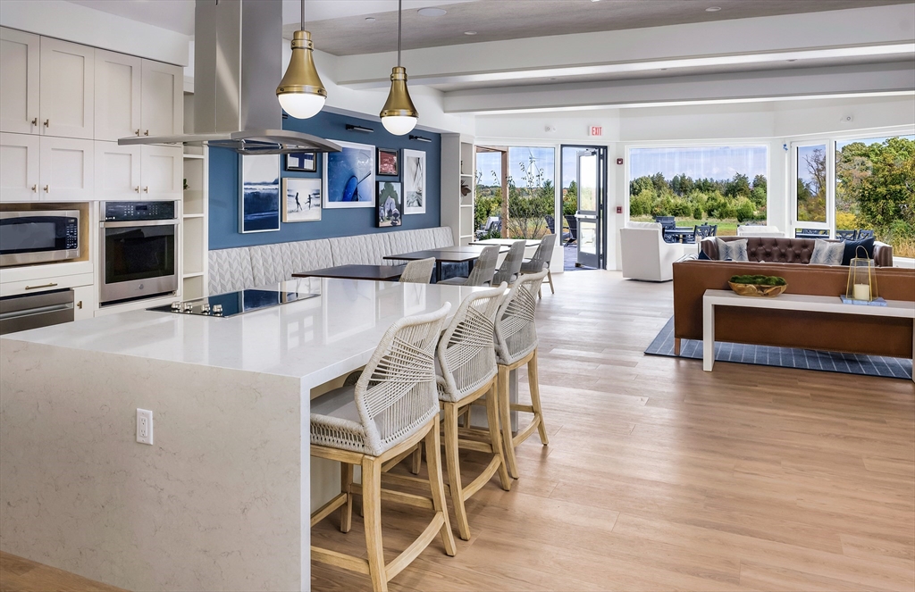 130 Chief Justice Cushing Highway, Unit 213 Scituate, MA 02066 - Photo 39 of 40 a dining hall with stainless steel appliances granite countertop a stove a kitchen island a dining table and chairs with wooden floor