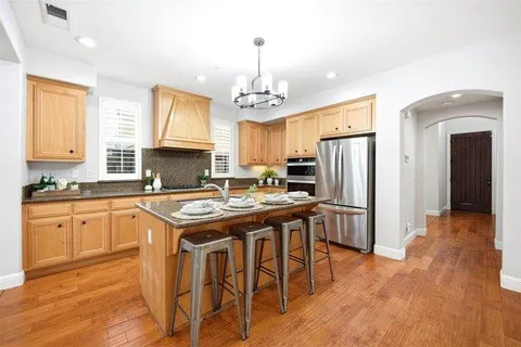 a kitchen with stainless steel appliances granite countertop a refrigerator a sink dishwasher a stove and white countertops with wooden floor