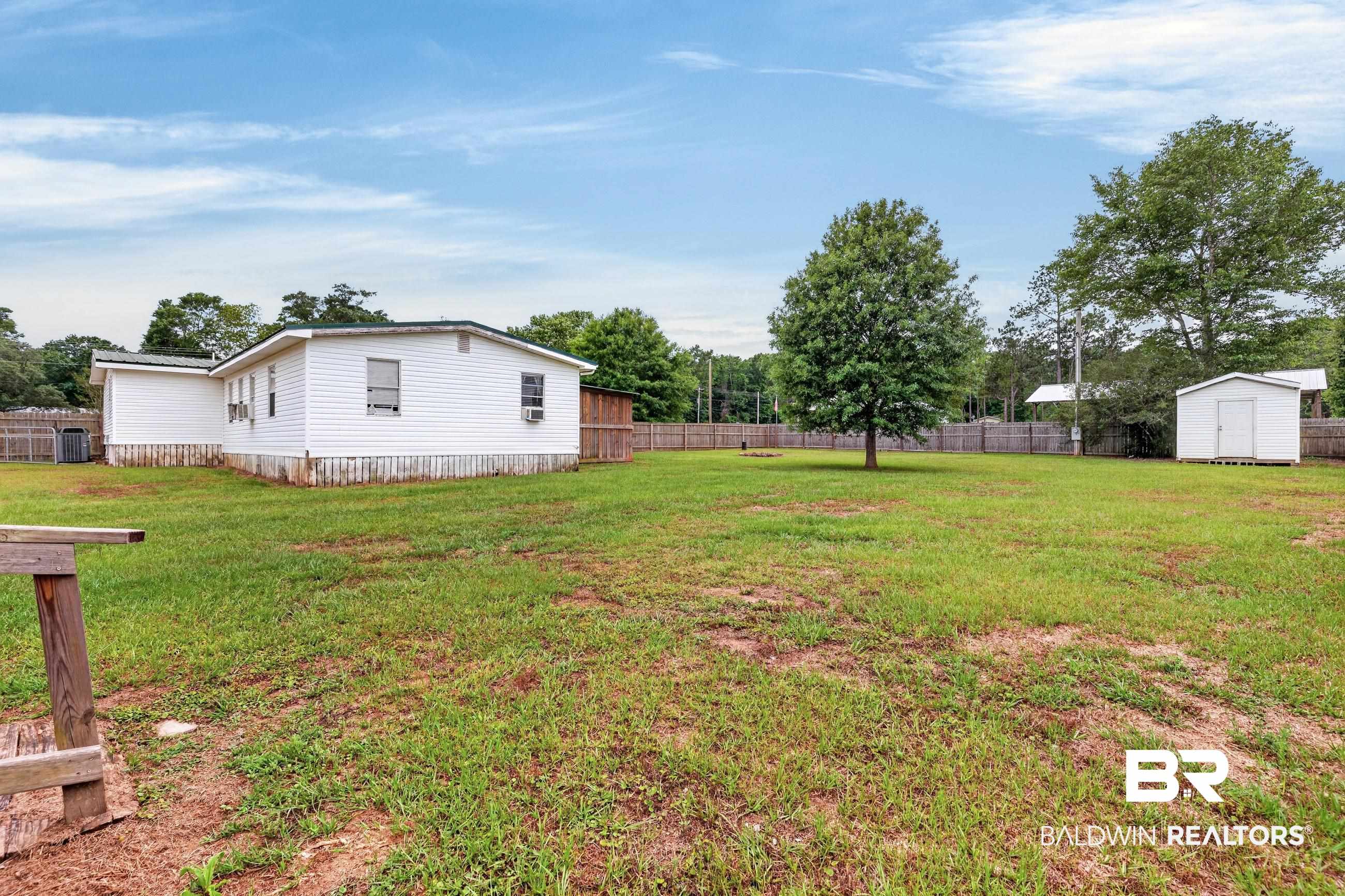 24903 Patterson Road Robertsdale, AL 36567 - Photo 12 of 57 Expansive rear yard featuring a white-sided residence, a separate storage shed, a mature shade tree, and perimeter fencing