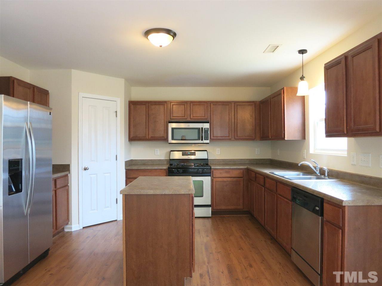 6714 Harter Court Raleigh, NC 27610 - Photo 6 of 25 The spacious Kitchen features lots of wood cabinets, HiMacs granite-look laminate ctrs, stainless steel appliances (gas range, MW, DW), island & WI Pantry closet.