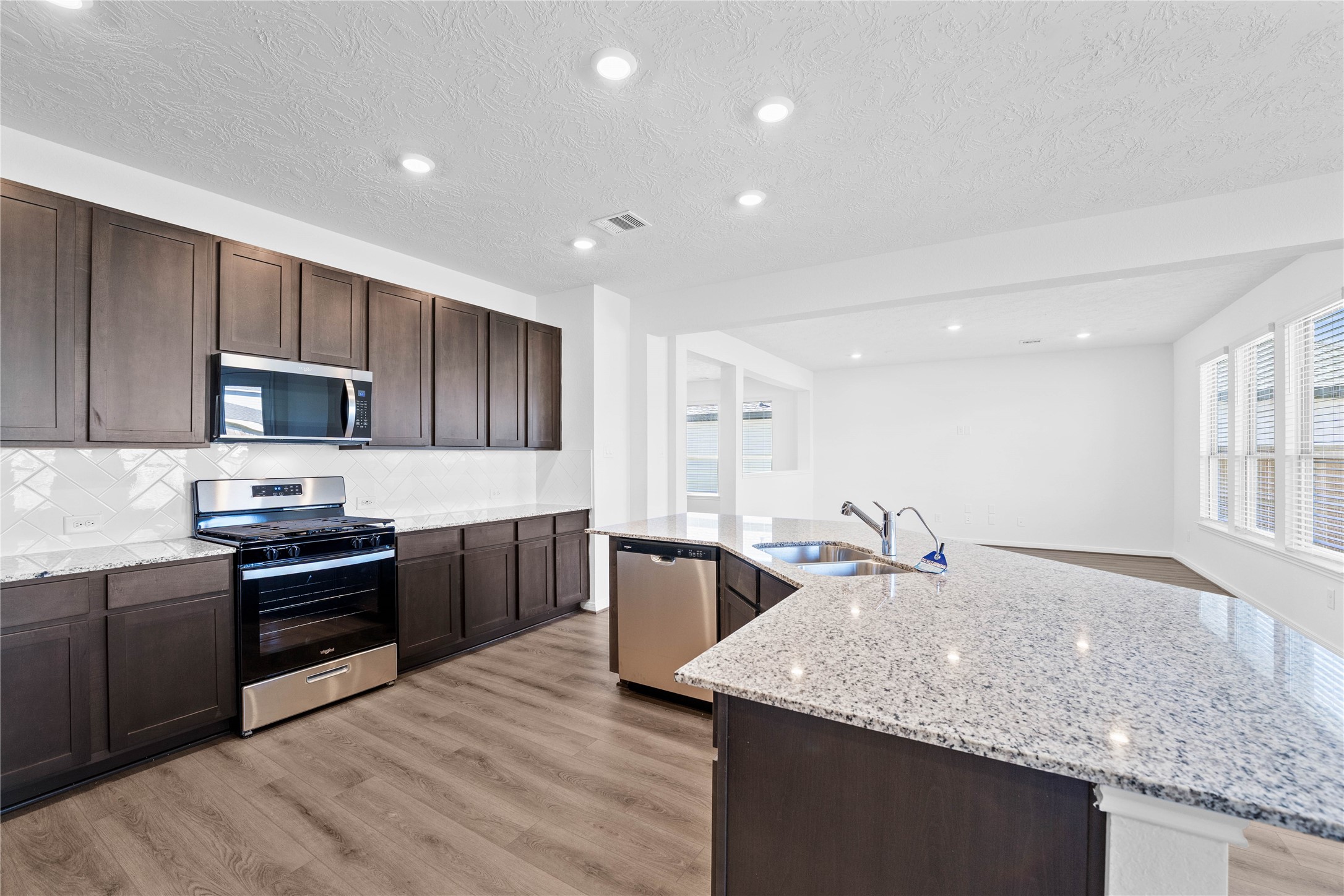 3519 Rocky Aspen Dr Spring Spring, TX 77373 - Photo 10 of 29 This spacious kitchen boasts soaring ceilings, Woodmont Dakota cabinets in a Smoke stain, Granite Luna Pearl countertops, stainless steel Whirlpool appliances, a modern Daltile backsplash, recessed lighting, an extended breakfast bar countertop, and a pantry—all overlooking the expansive family room and breakfast nook.