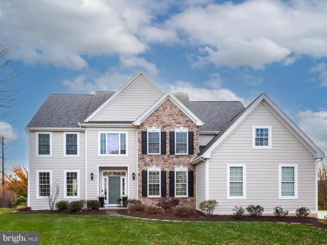 a view of a white house next to a yard with big trees and plants