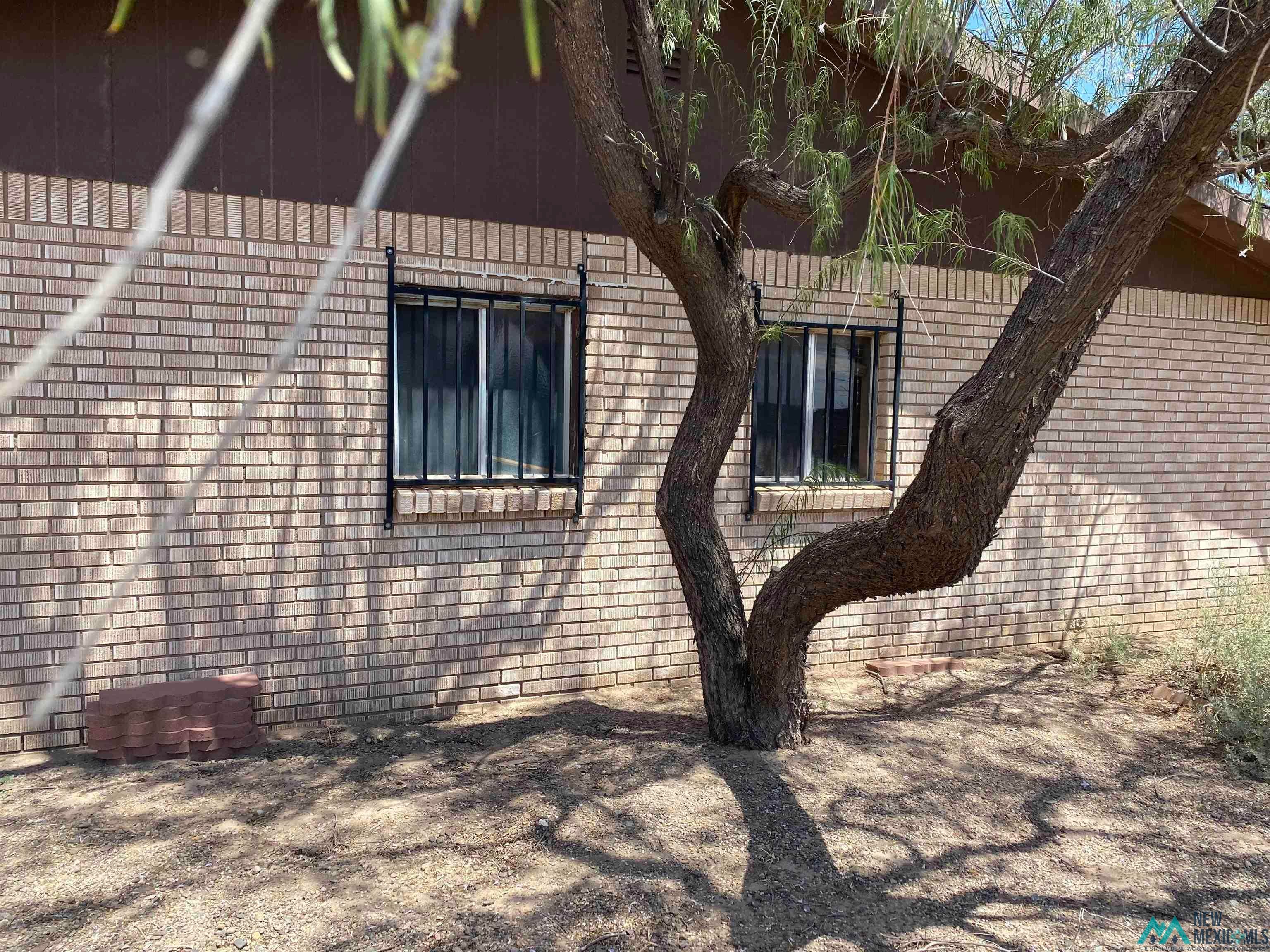 5985 Charolais Road Deming, NM 88030 - Photo 4 of 22 Brick exterior featuring two windows with security bars, shaded by a mature tree