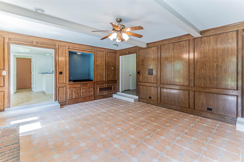 127 Nicklaus Nook Lancaster, TX 75146 - Photo 6 of 37 Unfurnished living room with a ceiling fan, beamed ceiling, wood walls, and a decorative wall