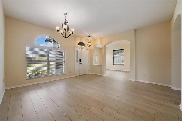 an empty room with wooden floor chandelier and windows