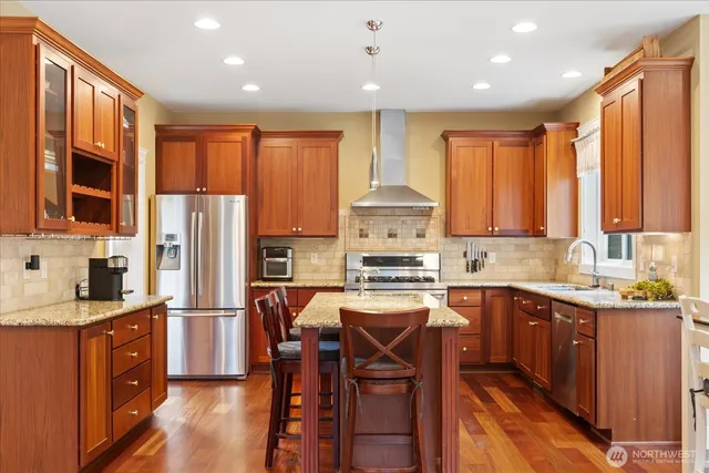 a kitchen with stainless steel appliances granite countertop a refrigerator a sink dishwasher a stove and white countertops with wooden cabinets