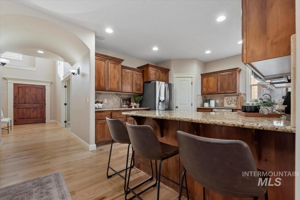 1082 East Azan Street Meridian, ID 83646 - Photo 7 of 47 Kitchen with light stone countertops, wood finish cabinetry, a kitchen breakfast bar, light wood-style floors, and decorative backsplash