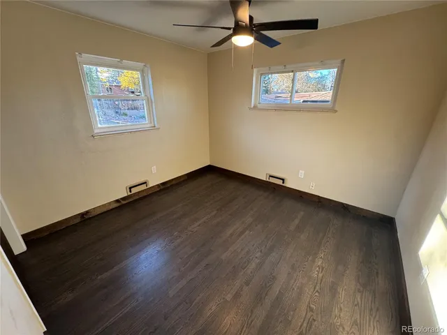 an empty room with wooden floor ceiling fan and windows
