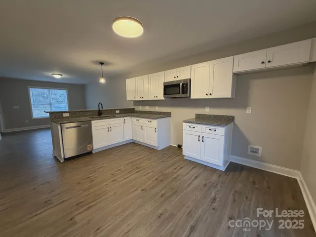 a kitchen with stainless steel appliances granite countertop a stove top oven a sink and white cabinets with wooden floor