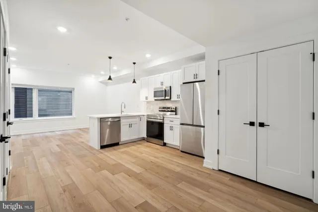 a large white kitchen with granite countertop a stove a sink dishwasher a refrigerator and white cabinets with wooden floor