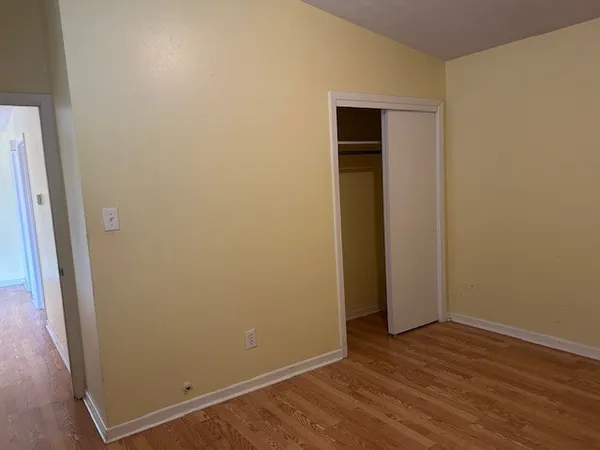 a view of an empty room with wooden floor and closet