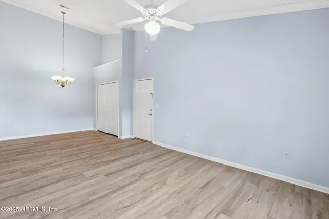 a view of an empty room with wooden floor and a ceiling fan