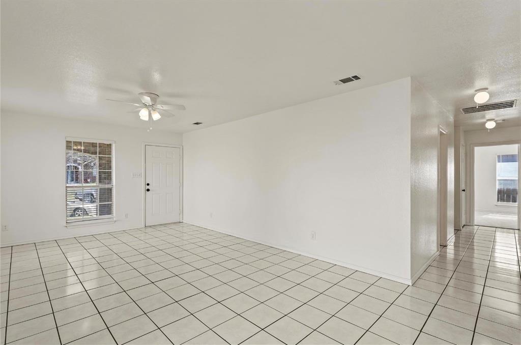 5169 East Rim Road Dallas, TX 75211 - Photo 9 of 19 Spacious room featuring white tile flooring, a multi-pane window, a ceiling fan with integrated lighting, and a white entry door