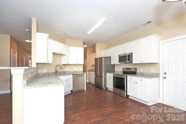 a large kitchen with a stove top oven a sink dishwasher a refrigerator and white cabinets with wooden floor