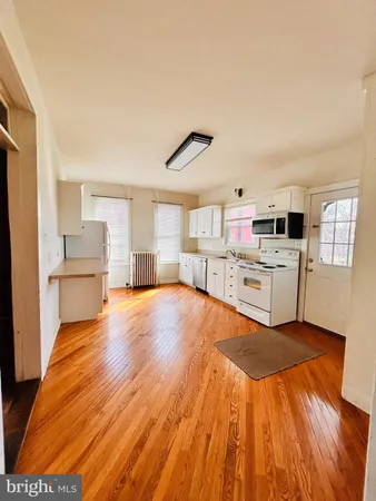 a large white kitchen with kitchen island a stove a refrigerator cabinets and a wooden floor