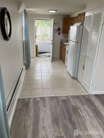 a view of a refrigerator in kitchen and an empty room with wooden floor