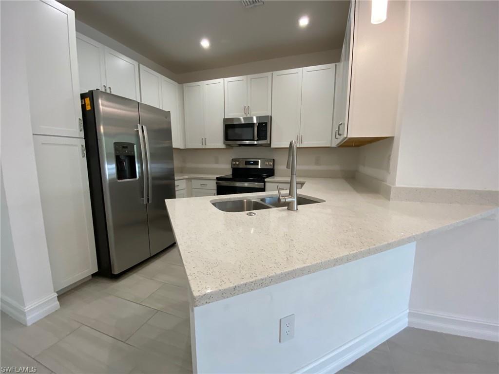 7530 Rockefeller Drive Naples, FL 34119 - Photo 2 of 18 Modern kitchen featuring white shaker cabinetry, stainless steel appliances, speckled quartz countertops, and a double basin sink with a gooseneck faucet