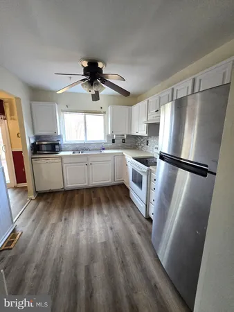 a kitchen with stainless steel appliances granite countertop a refrigerator a sink dishwasher a stove and white countertops with wooden floor
