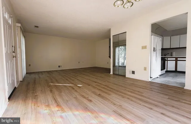 an empty room with wooden floor and a kitchen view