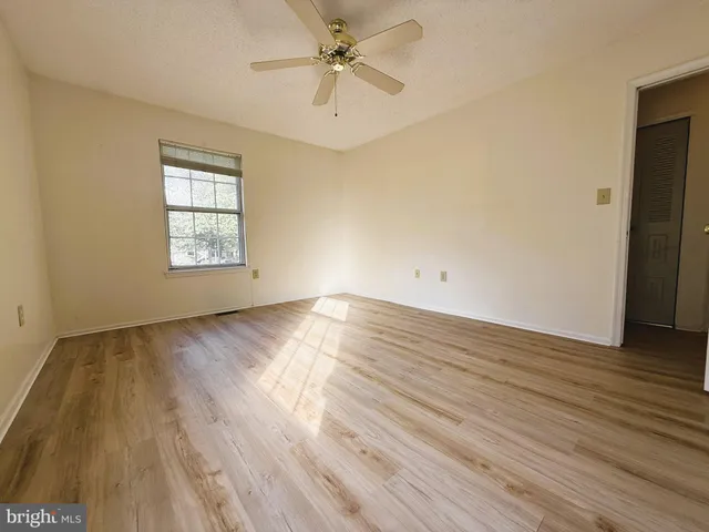 an empty room with wooden floor chandelier fan and windows