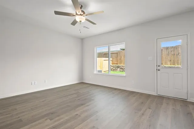 an empty room with wooden floor chandelier fan and windows