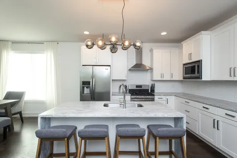 a kitchen with stainless steel appliances granite countertop a dining table chairs refrigerator and cabinets