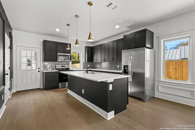 a kitchen with stainless steel appliances a refrigerator a sink dishwasher a oven and a dining table with wooden floor