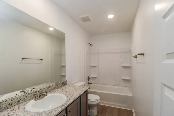 a bathroom with a granite countertop sink a toilet a mirror and shower