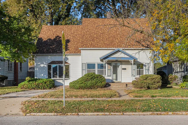 a view of a white house next to a yard with large trees