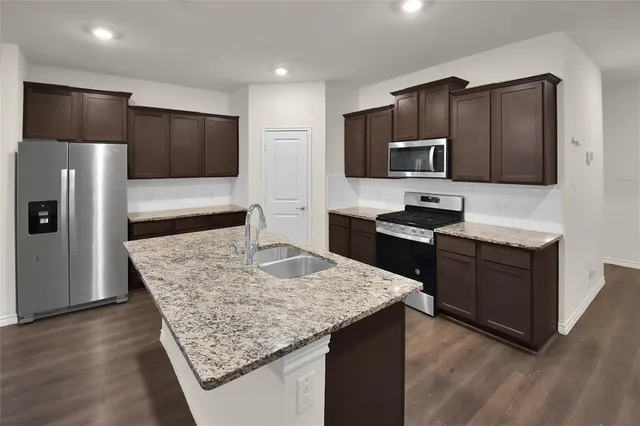 a kitchen with kitchen island granite countertop stainless steel appliances a sink stove refrigerator and cabinets