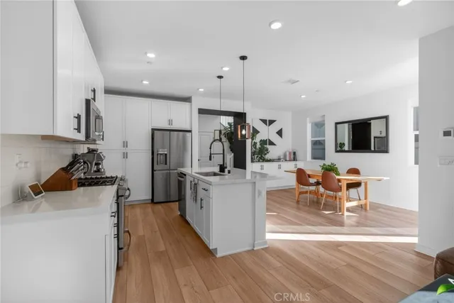 a kitchen with stainless steel appliances kitchen island granite countertop a refrigerator a oven a sink and white cabinets with wooden floor