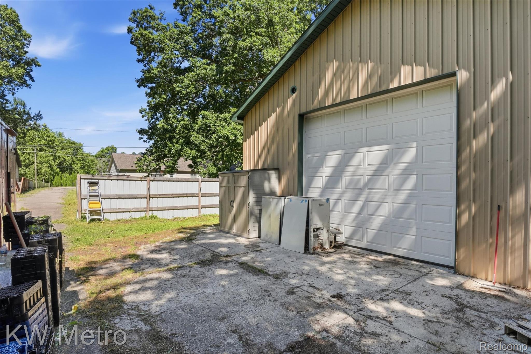 22733 Sumpter Road Belleville, MI 48111 - Photo 35 of 52 Metal-sided structure featuring a large white paneled garage door, green-trimmed roofline, and a concrete driveway leading to a fenced perimeter