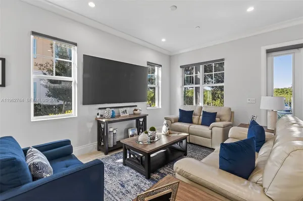 a living room with stainless steel appliances furniture a dining table wooden floor and a view of kitchen