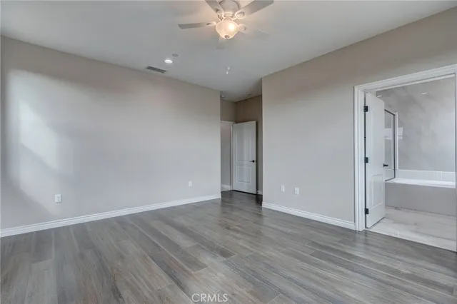a view of an empty room with wooden floor and a ceiling fan