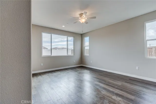 an empty room with wooden floor chandelier fan and windows