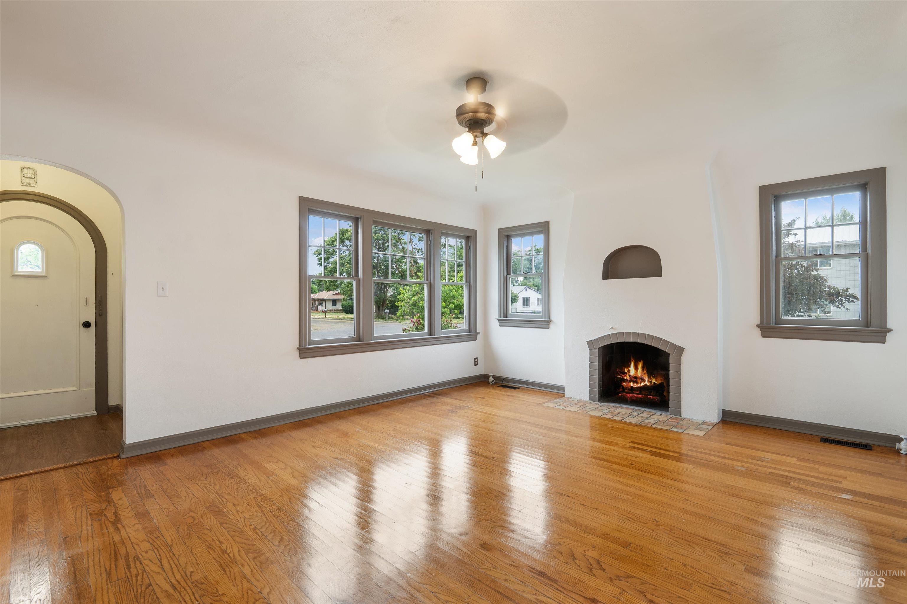 191 Southwest 5th Avenue Ontario, OR 97914 - Photo 7 of 50 Unfurnished living room featuring light wood-style flooring, a brick fireplace, a ceiling fan, and arched walkways