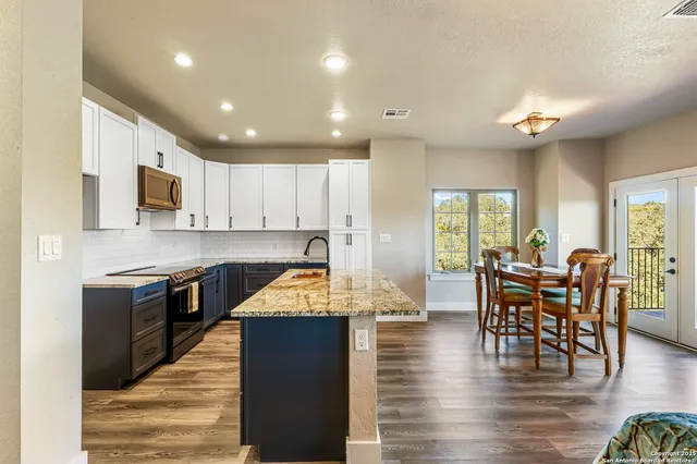 a kitchen with stainless steel appliances granite countertop wooden floor a stove top oven a dining table and chairs with wooden floor