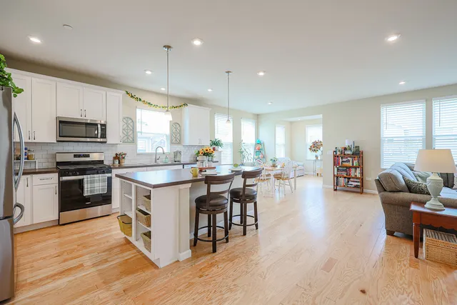 a kitchen with kitchen island stainless steel appliances a dining table chairs sink and wooden floor