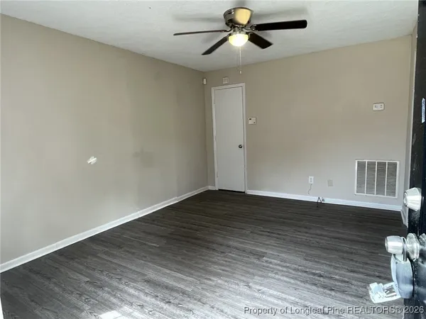 a view of an empty room with wooden floor and a ceiling fan