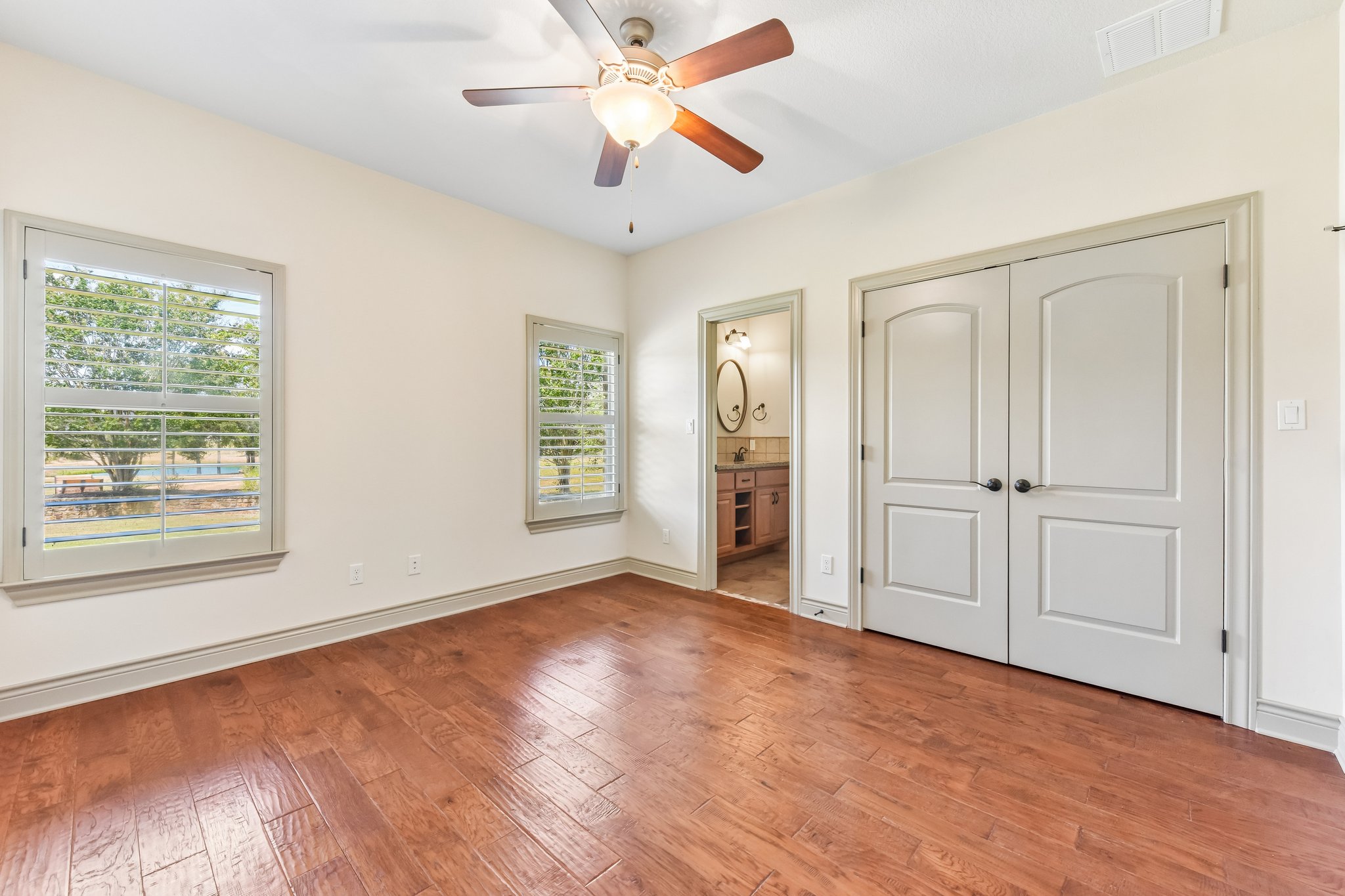 163 Powder Horn Road Bastrop, TX 78602 - Photo 18 of 34 Rich hardwood flooring complements the neutral walls and plantation shutters in this tranquil bedroom.