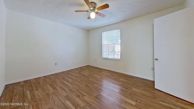 an empty room with wooden floor fan and windows