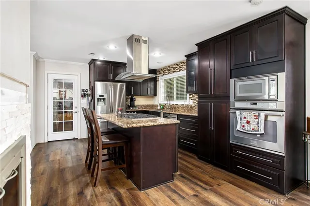 a kitchen with stainless steel appliances kitchen island granite countertop a refrigerator a stove and a wooden cabinets