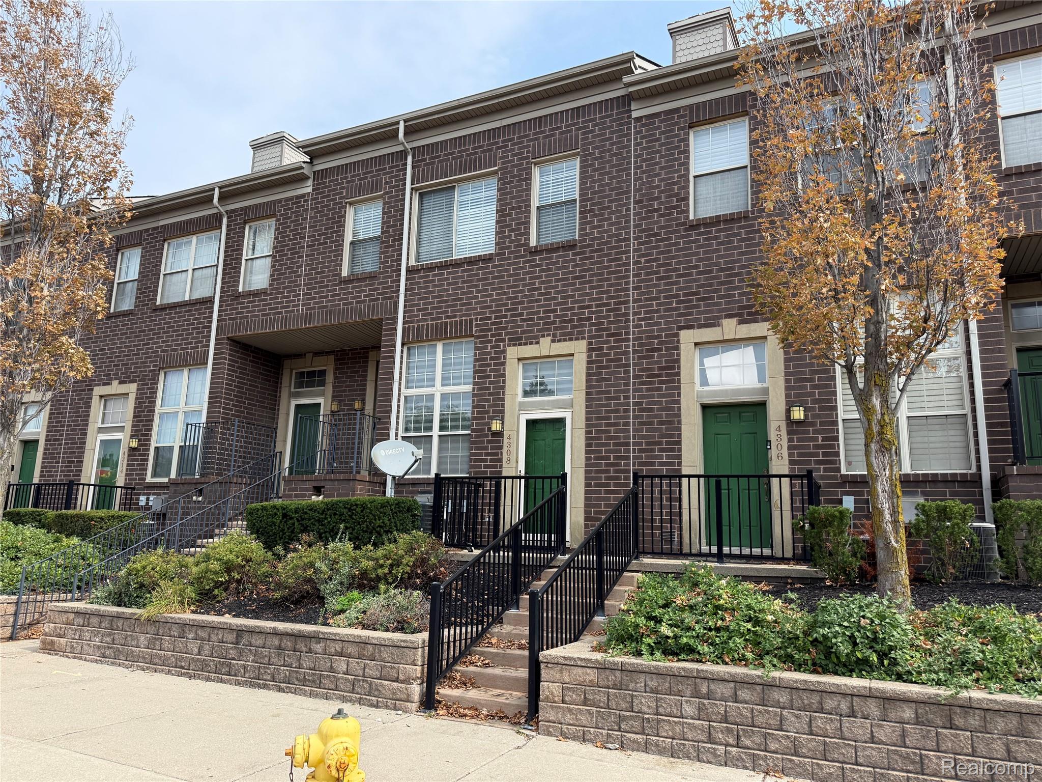 4308 Schaefer Road Dearborn, MI 48126 - Photo 1 of 11 Brown brick facade featuring multiple windows with light-colored sills, green entry doors, and black metal railings leading to separate entrances
