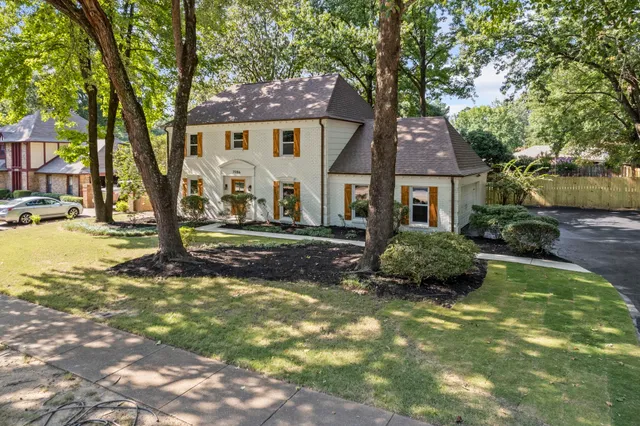 a view of a white house next to a yard with big trees