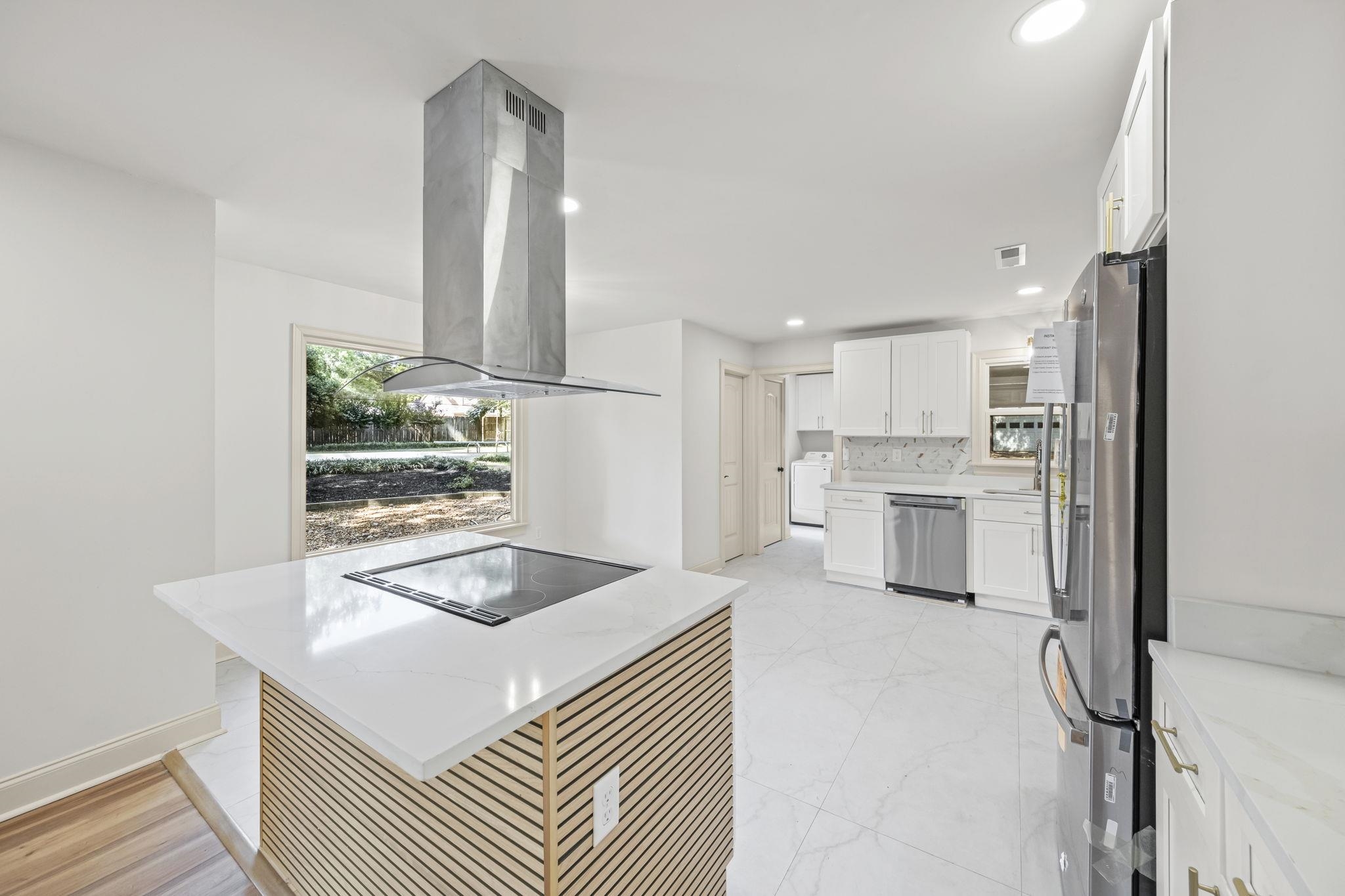 Kitchen featuring island range hood, light marble finish floors, appliances with stainless steel finishes, white cabinetry, and decorative backsplash