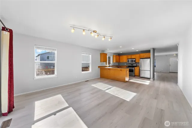 a view of an empty room with kitchen and window