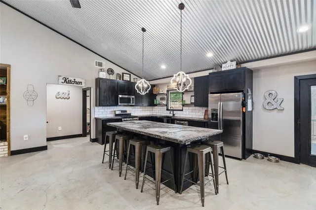 a kitchen with stainless steel appliances kitchen island granite countertop a table chairs sink and cabinets
